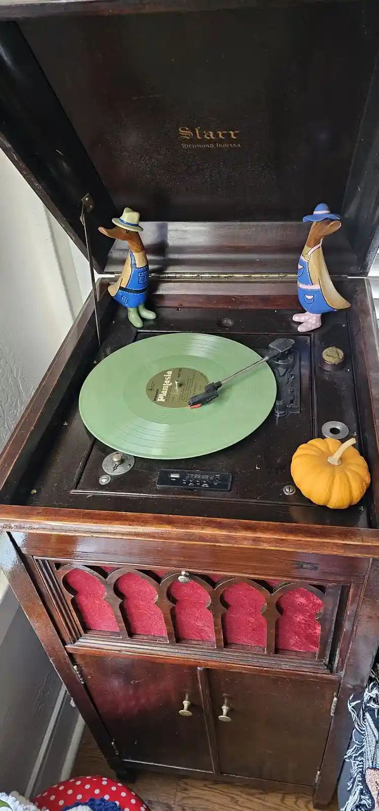 A vintage wooden record player with a green vinyl record labeled 'Plantasia' spinning on the turntable, flanked by two…