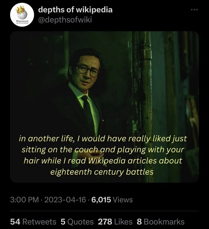 A man in a suit and glasses stands in a dimly lit, green-tinted hallway, looking directly at the camera with a calm…