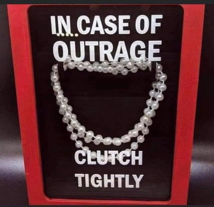 A red-framed display case with a black background shows a pearl necklace arranged in the shape of a hand clutching…