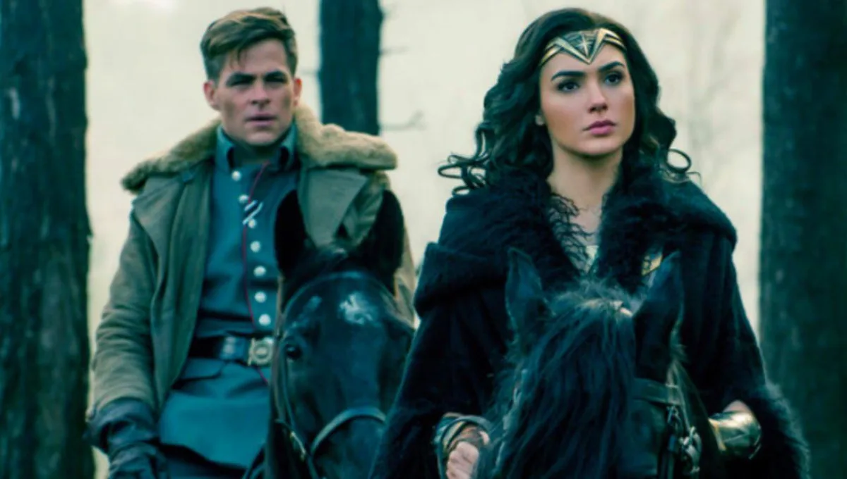 A still from a movie shows two people riding horses through a forest. The person on the left, a man in a military-style…