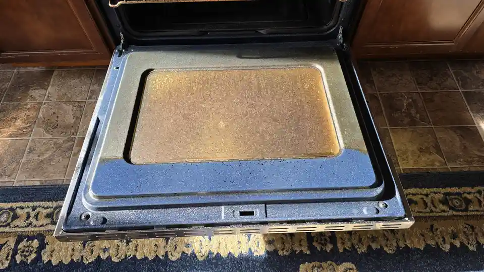 A top-down view of a heavily soiled oven interior, with the bottom surface covered in a thick layer of baked-on brown…