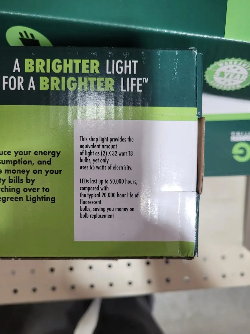 A close-up photo of a green product box for an LED shop light, showing text that claims the light provides the brightness of…
