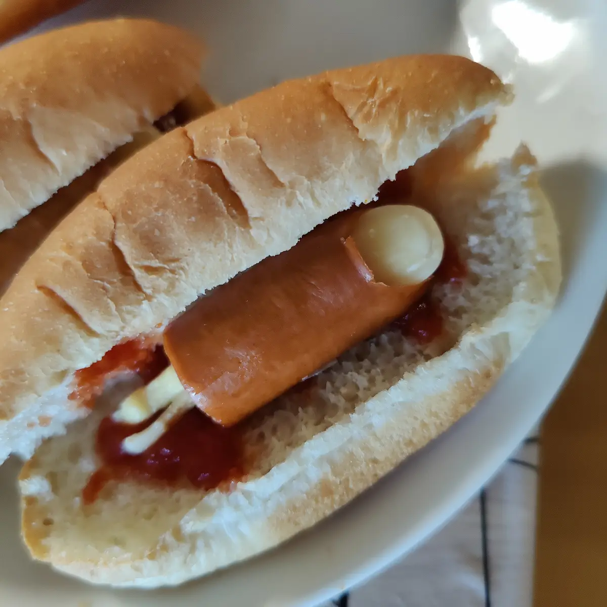A close-up photo of a hot dog in a bun with ketchup and mustard, where the hot dog has a white, rounded protrusion…