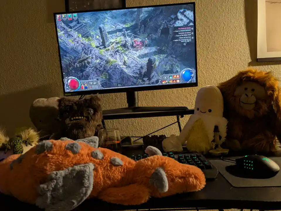 A dimly lit gaming setup shows a monitor displaying a Diablo game with a character fighting monsters. In front of the…