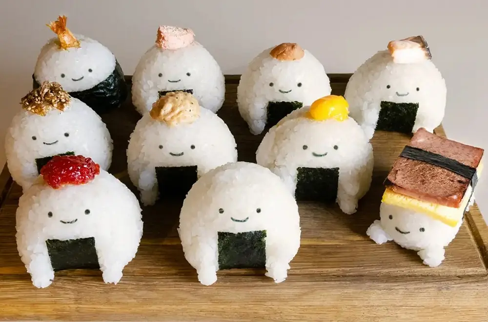 A group of cute, smiling onigiri (rice balls) with seaweed wraps and various toppings like fish roe, shrimp, and tamago…