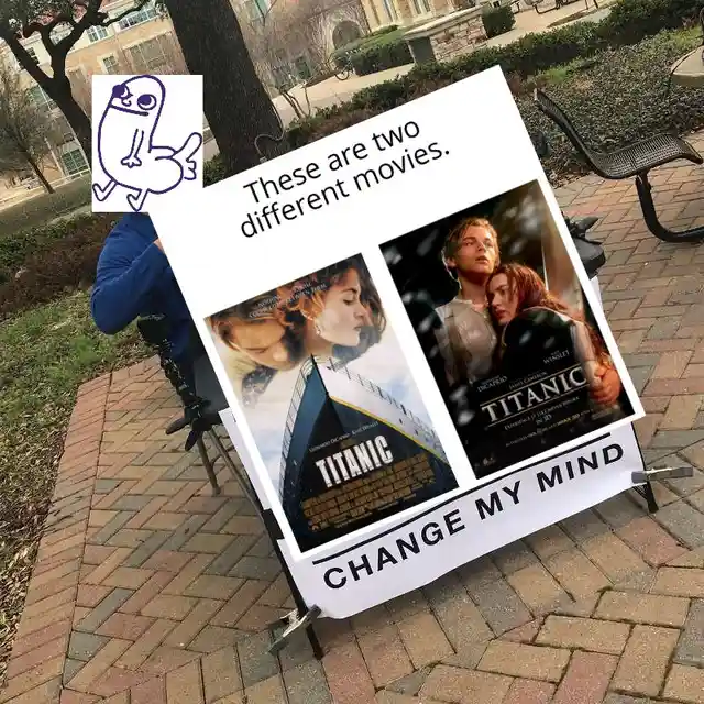 A person sits outdoors holding a large sign displaying two different movie posters for 'Titanic' side-by-side, one showing…