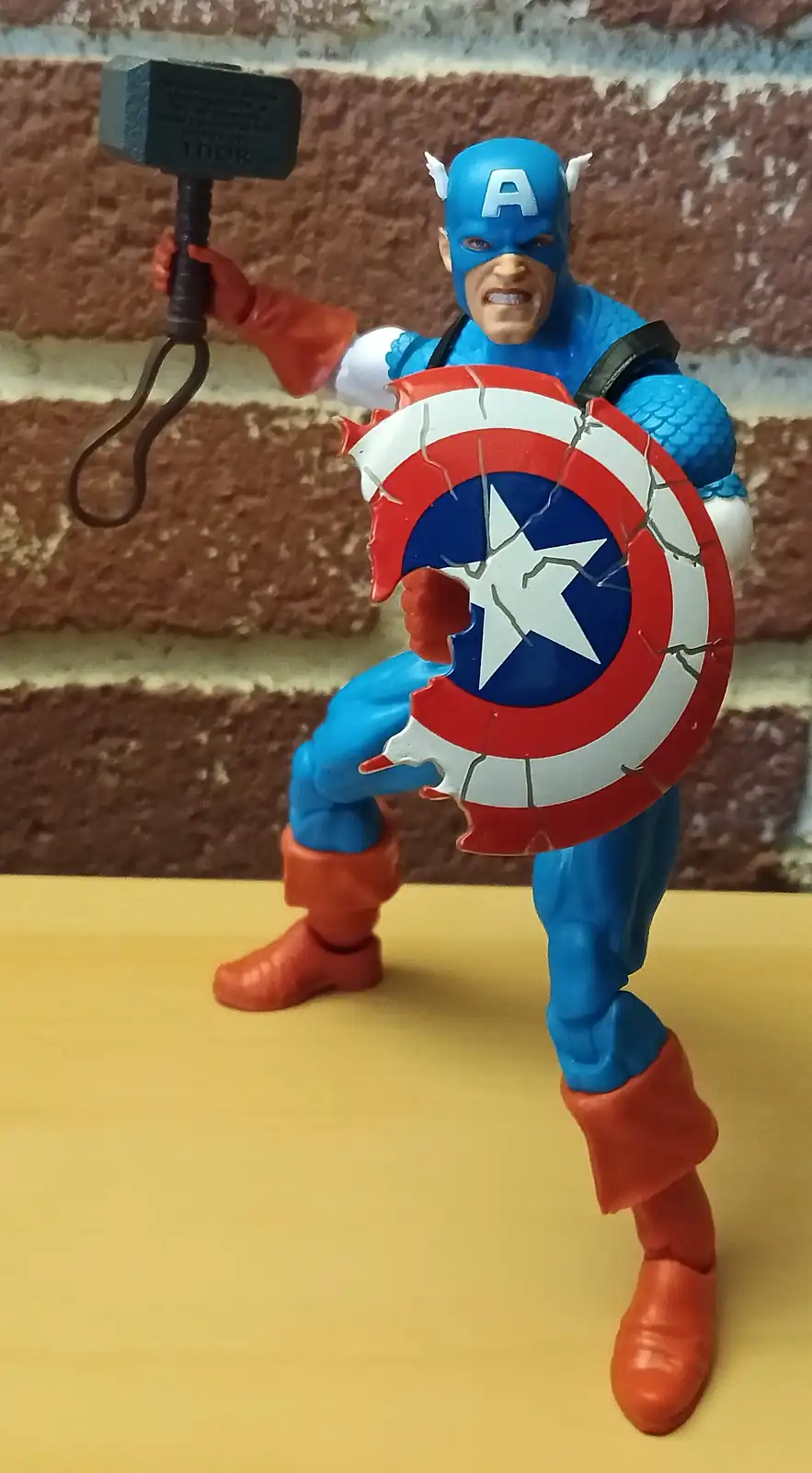 A Captain America action figure is posed holding Thor's hammer, Mjolnir, in one hand and his iconic shield in the other. The…