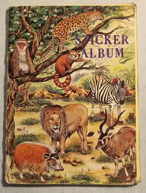 The image shows the cover of a vintage, worn sticker album featuring a colorful illustration of various African wildlife…