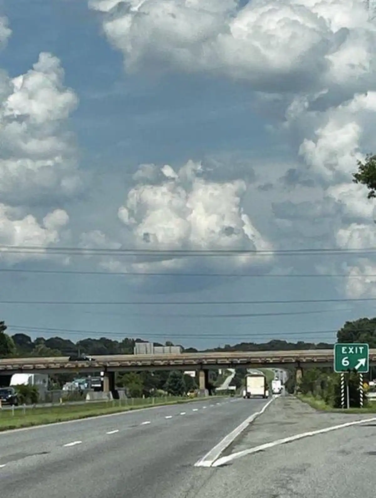 A highway scene with a green exit sign reading 'EXIT 6' on the right, a concrete overpass ahead, and a sky filled with…