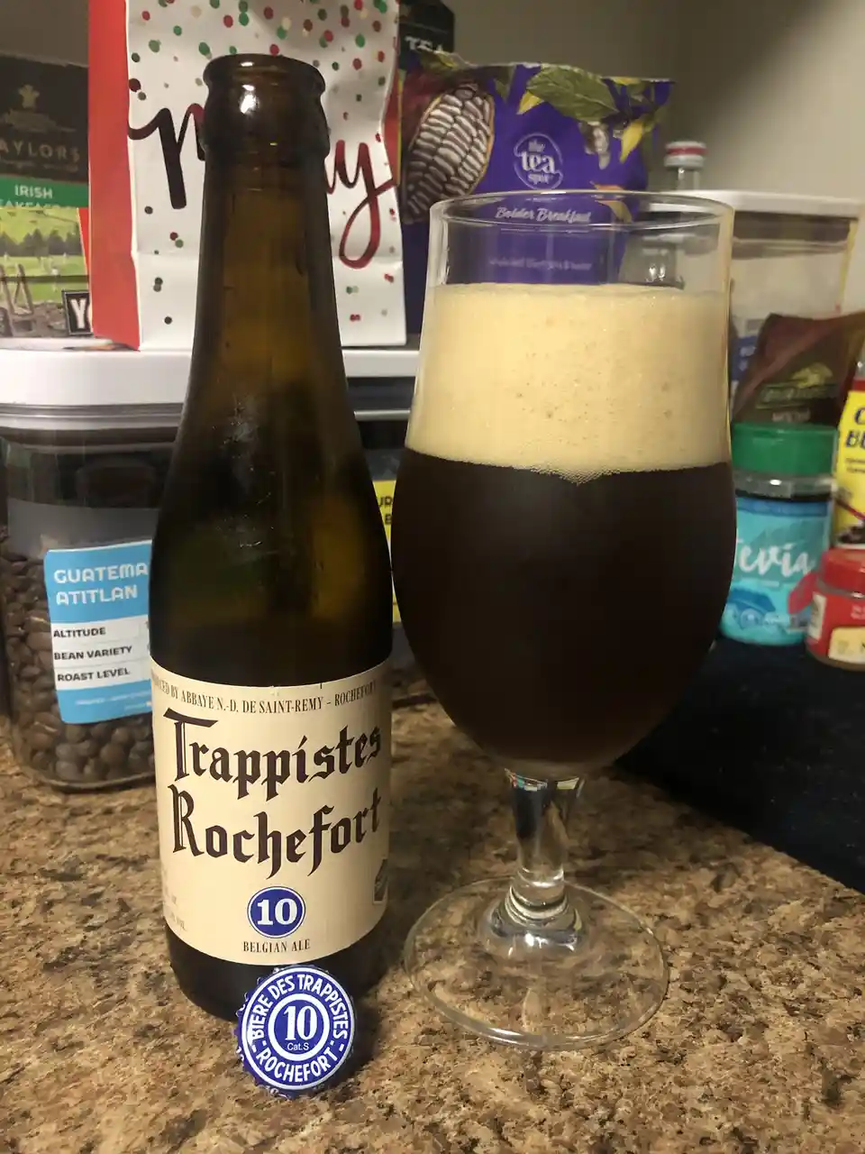 A bottle of Trappistes Rochefort 10 Belgian Ale sits next to a glass filled with the dark beer and a thick, creamy head…