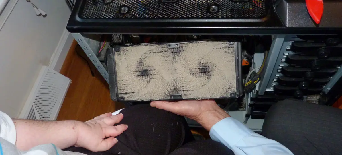 A person holds up a heavily clogged, dusty computer heatsink with visible dirt covering its fins, implying a shocking or…
