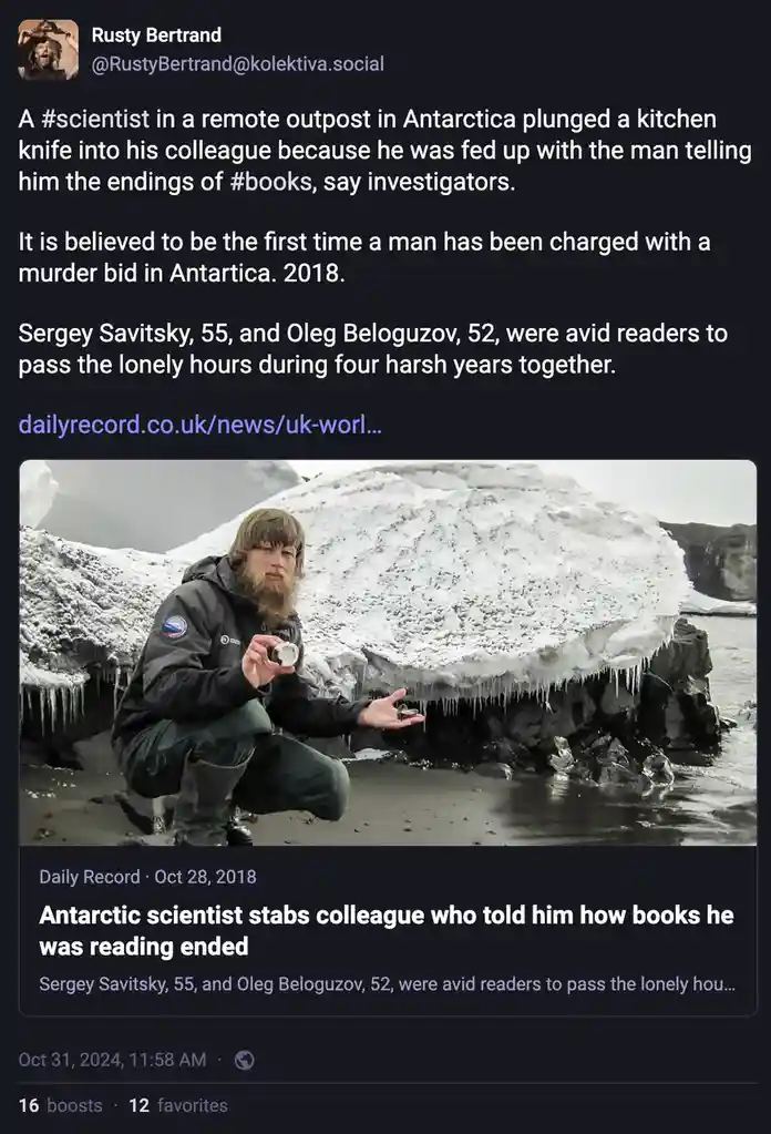 A man with a beard and winter gear crouches on a snowy, icy beach holding a rock sample, with a large ice-covered rock…