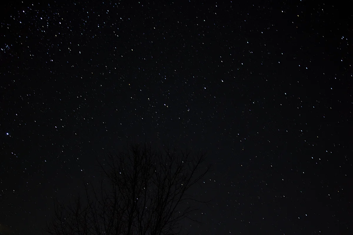 A long-exposure night sky photograph showing countless stars as streaks of light across a black canvas, with the dark…