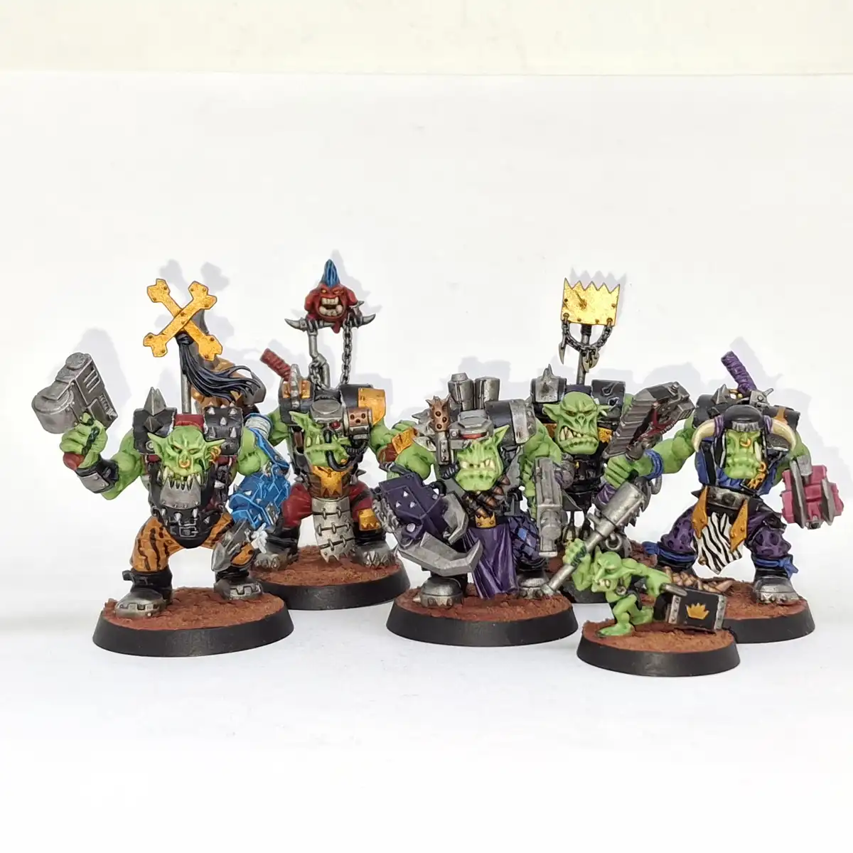 A group of five painted green orc miniatures, each holding different weapons and banners, stand on individual bases against…