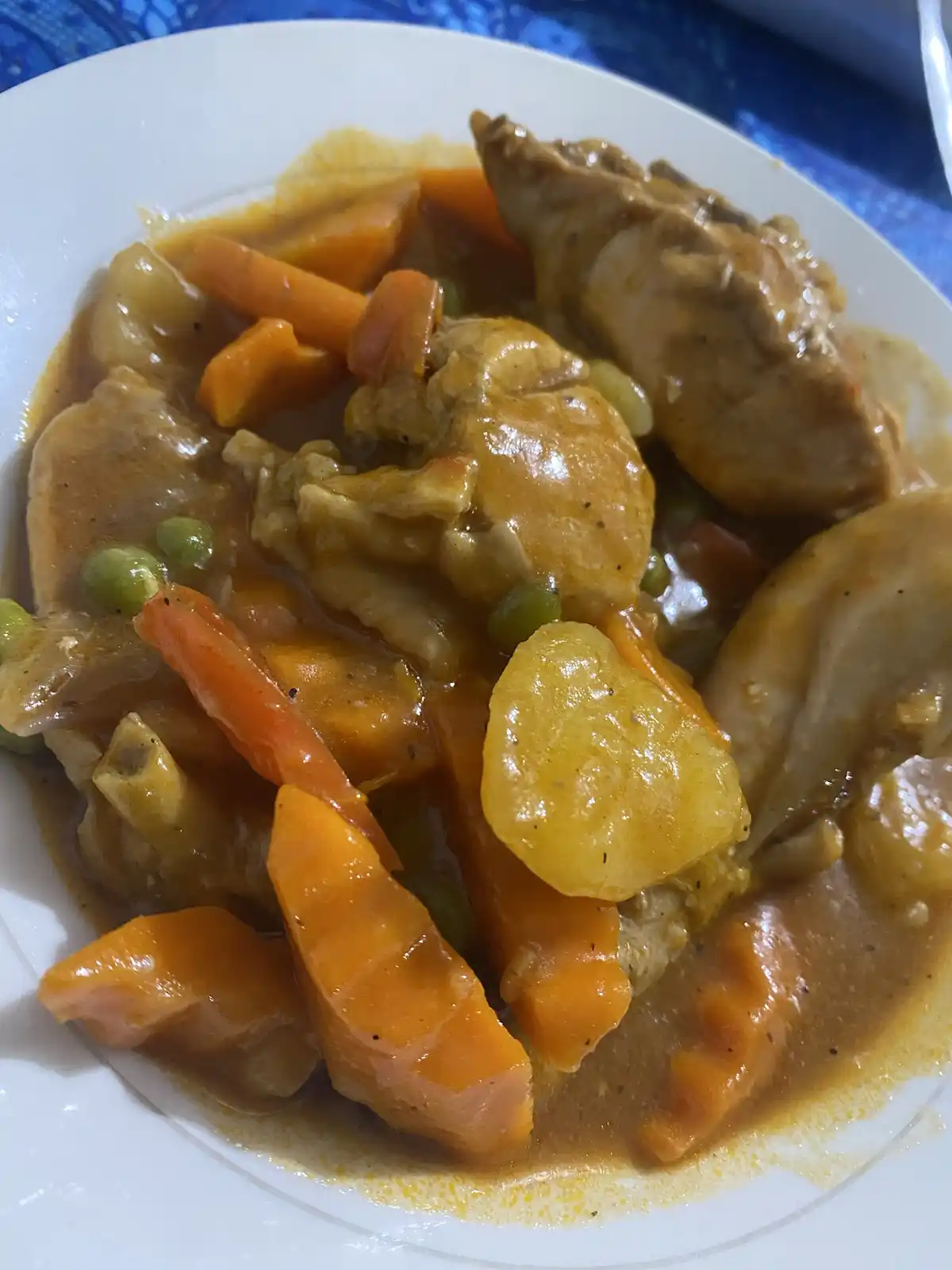 A close-up photo of a white plate filled with a stew-like dish containing chunks of chicken, orange carrot pieces, green…