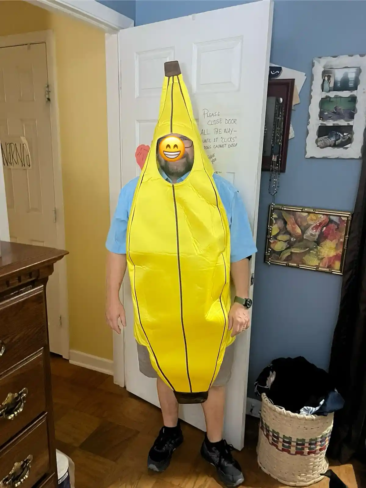 A man stands in a hallway wearing a full-body yellow banana costume with a black stem and black lines, his face obscured by…