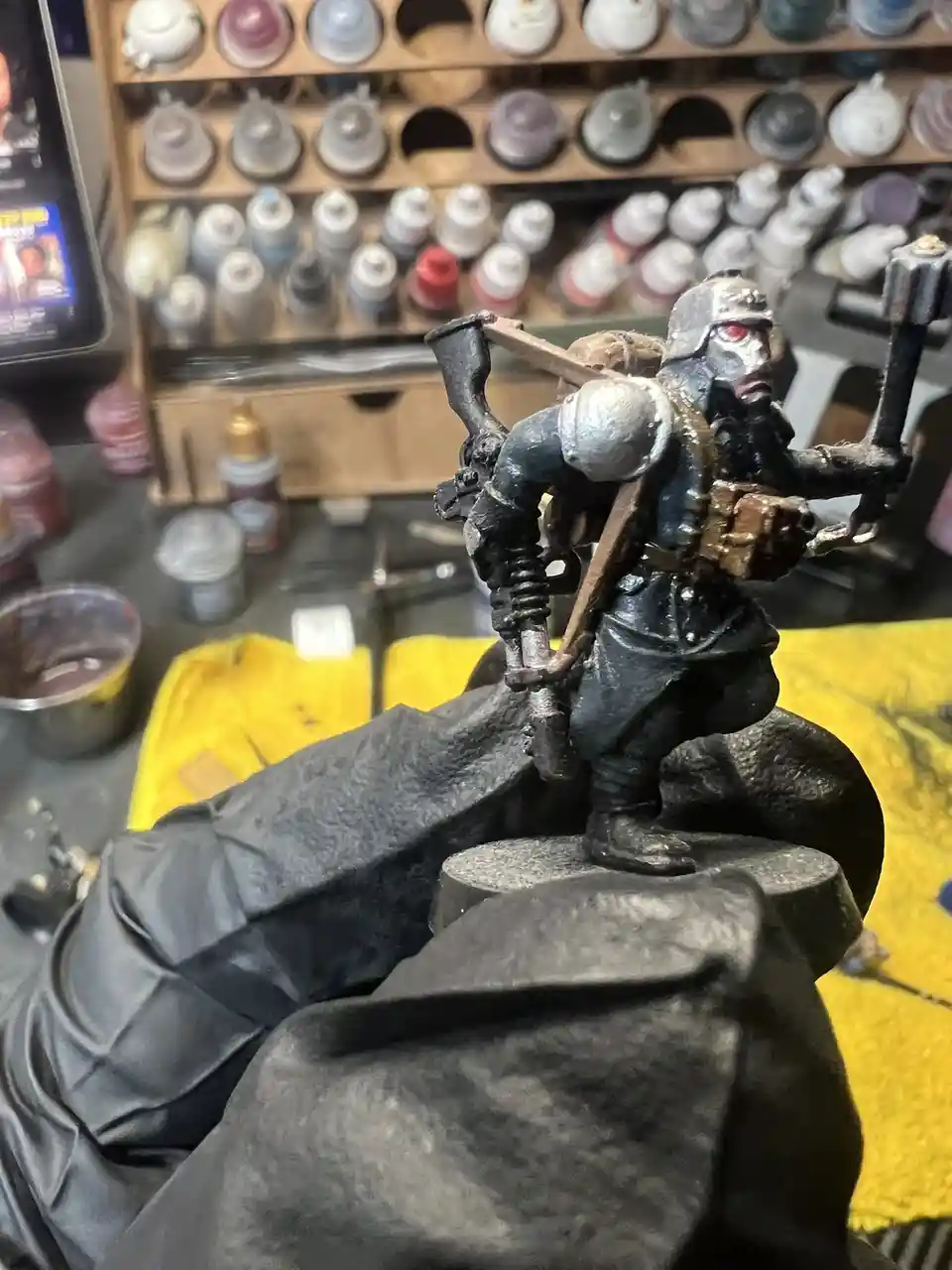 A close-up photo shows a heavily painted miniature figurine of a grim, armored warrior with a red eye, held in a gloved…