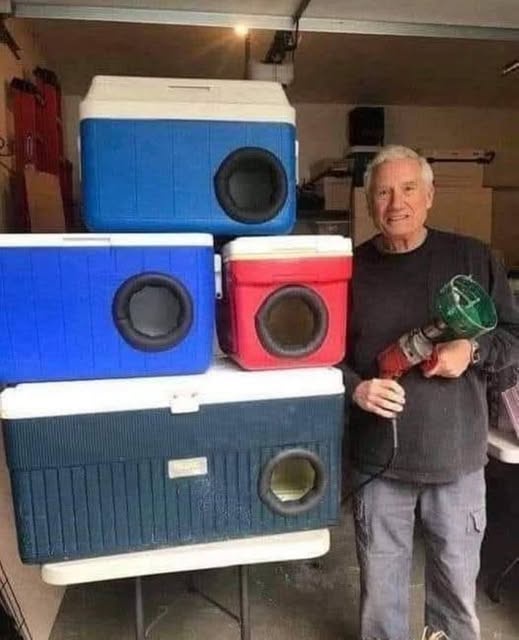 An older man stands in a garage next to a stack of four modified coolers, each with a circular hole cut into the side…