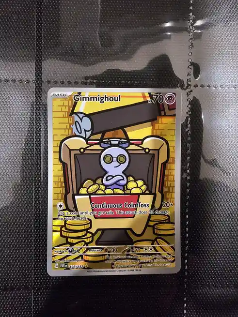 A Pokémon card featuring Gimmighoul, a ghost-type Pokémon sitting inside a treasure chest full of gold coins. The card's…