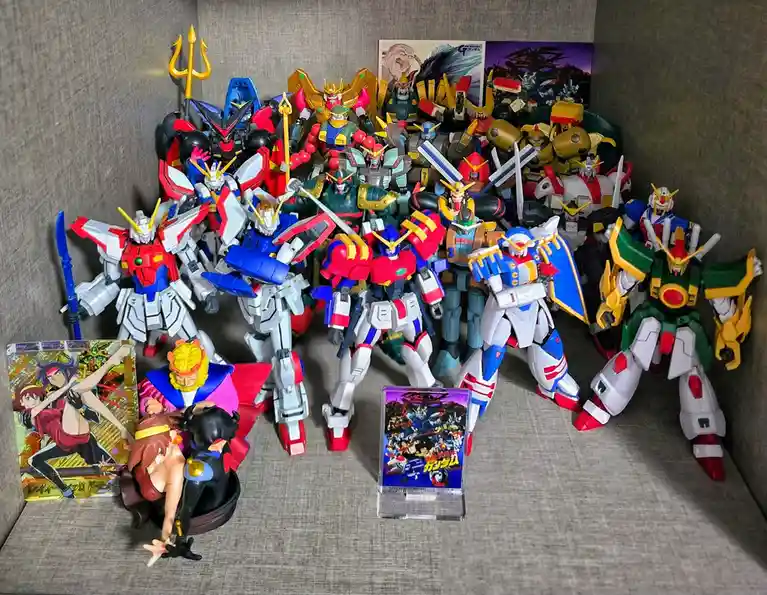 A large collection of colorful Gundam model kits and anime figures are displayed on a gray fabric surface, with some holding…