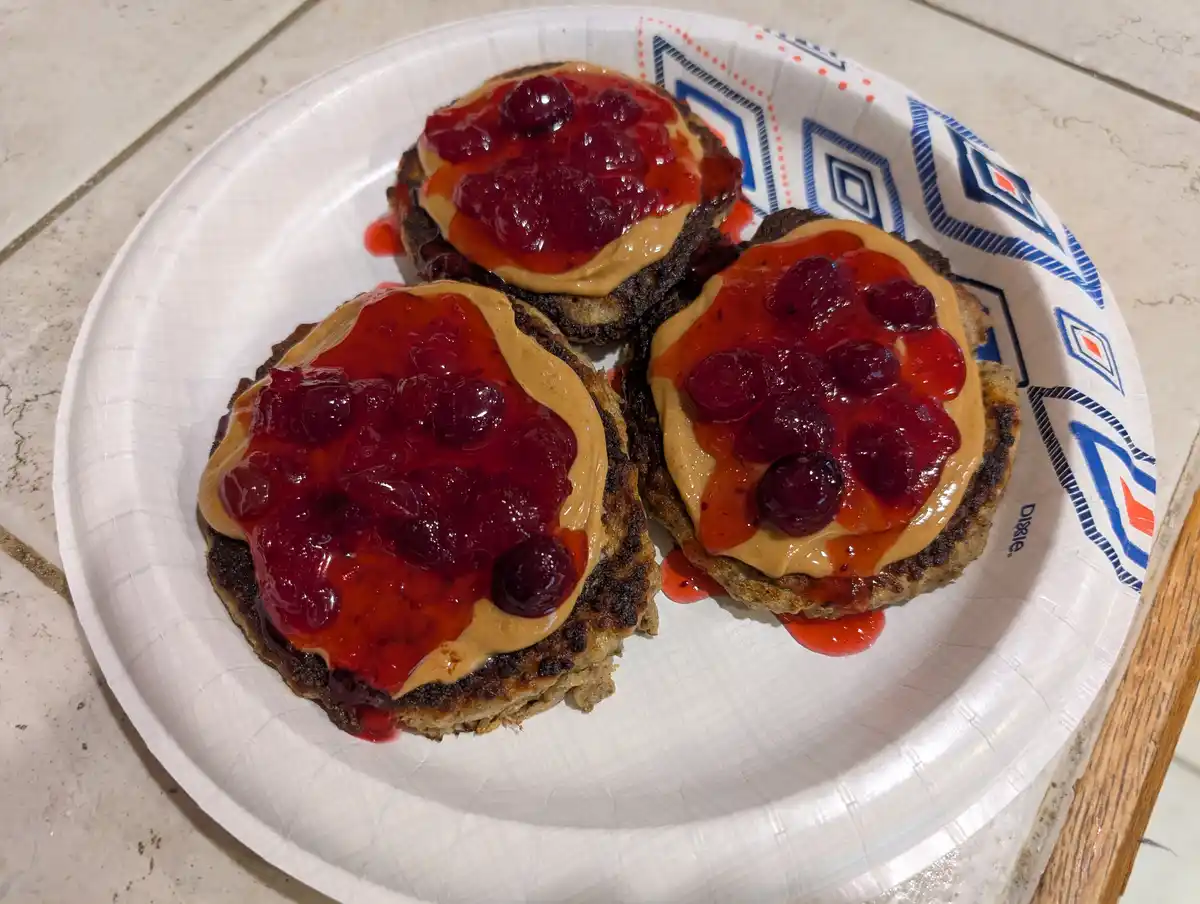 Three round pancakes on a white paper plate with blue and orange geometric patterns, each topped with a layer of peanut…