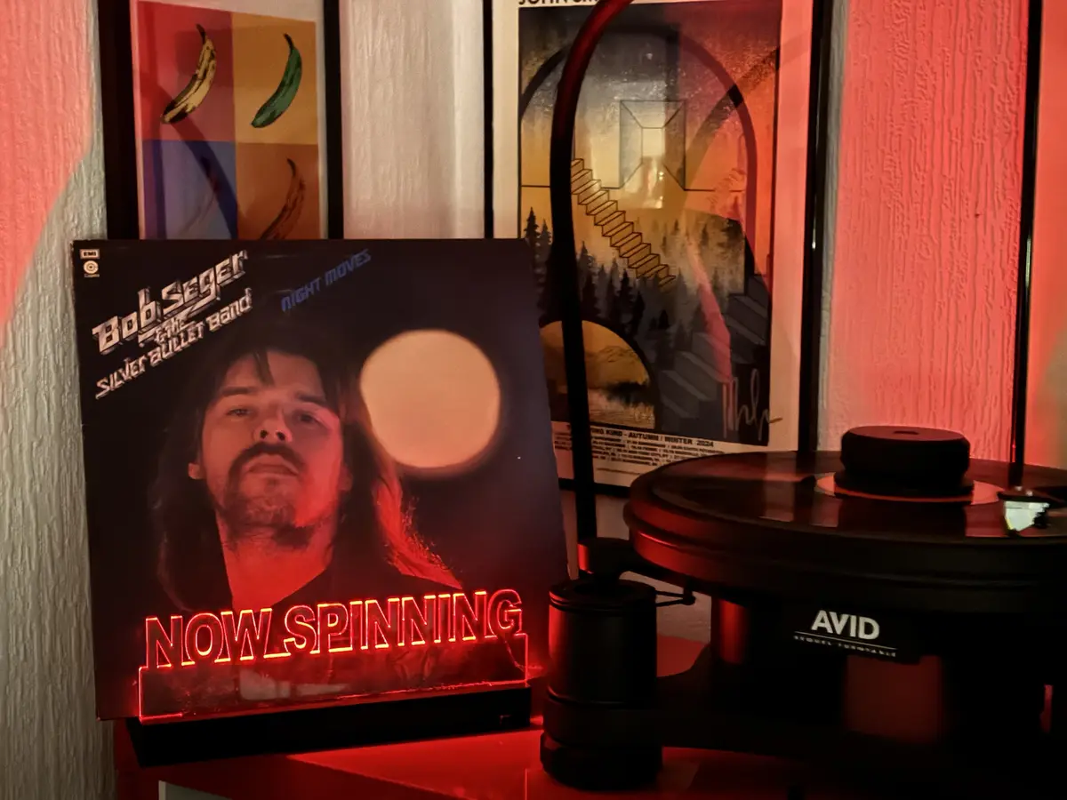 A vinyl record album cover for Bob Seger and the Silver Bullet Band's 'Night Moves' is displayed next to a turntable, with a…
