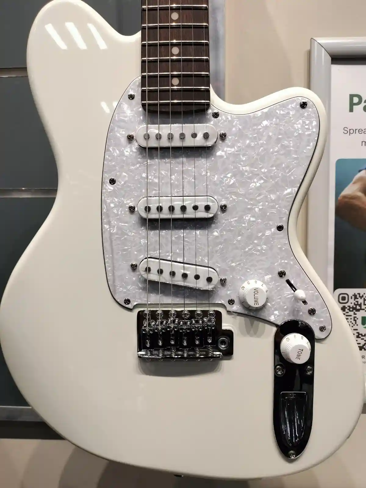 A close-up photo of a white electric guitar with a pearl pickguard, showing its volume and tone knobs. The overlaid text…