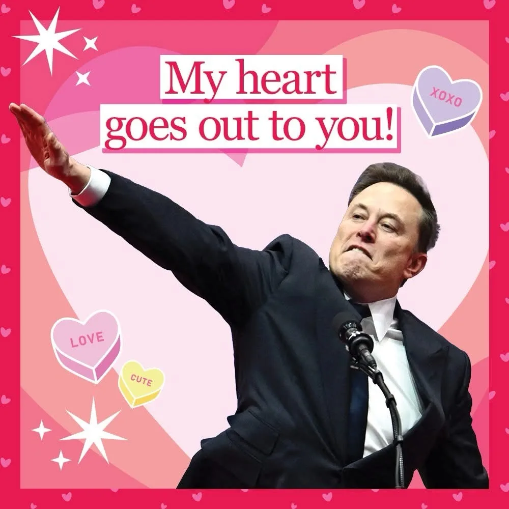A man in a dark suit stands at a microphone with his right arm raised, set against a pink background filled with hearts…