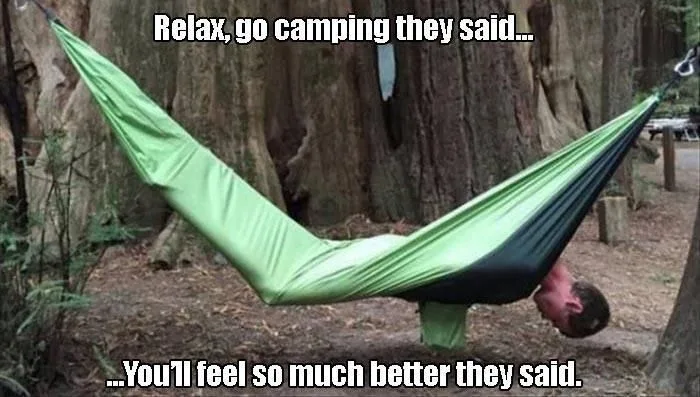A man is hanging upside down in a green and black hammock suspended between two trees in a wooded area. The overlaid text…