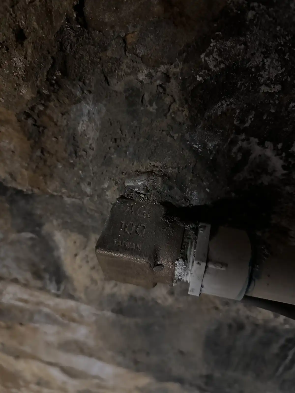 A close-up photo shows a dirty, dusty electrical outlet or junction box mounted in a rough, crumbling concrete wall. The…