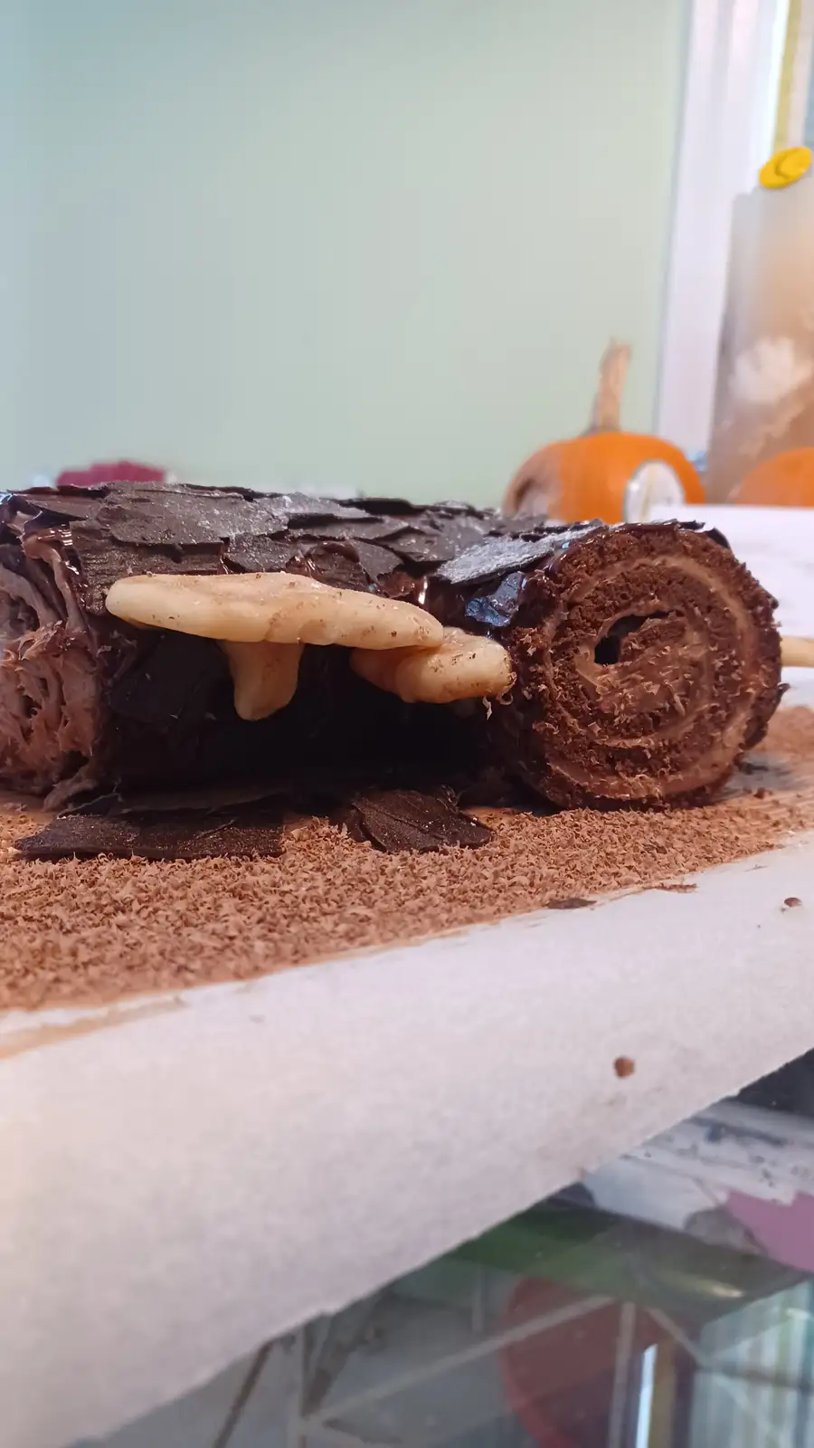 A chocolate cake roll decorated to resemble a log with edible mushrooms growing on it, placed on a surface dusted with cocoa…