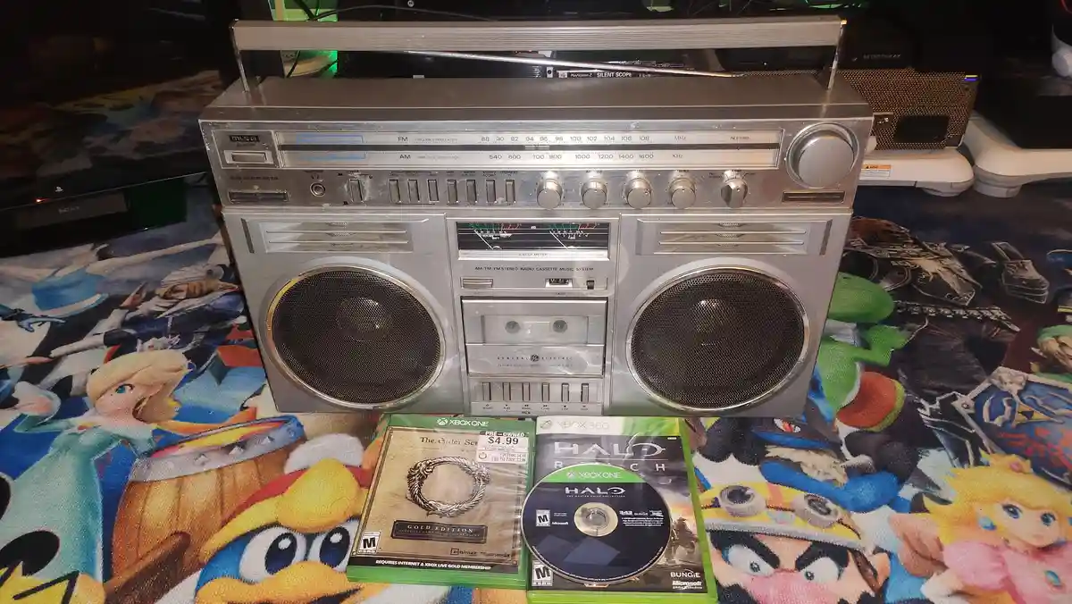 A vintage silver General Electric boombox with a telescoping antenna and cassette deck sits on a colorful rug featuring…