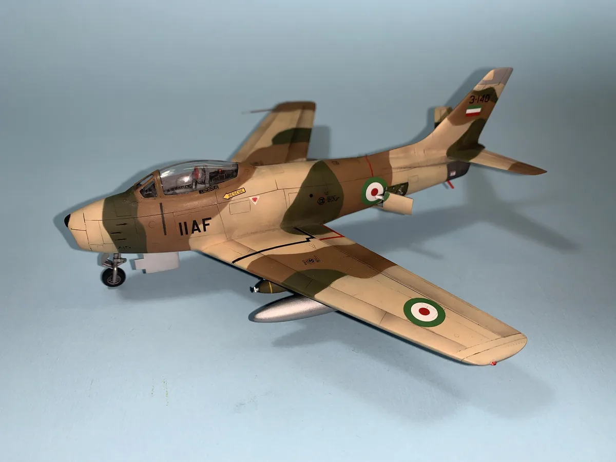 A detailed scale model of a military jet aircraft, painted in desert camouflage with markings including 'IIAF' on the…