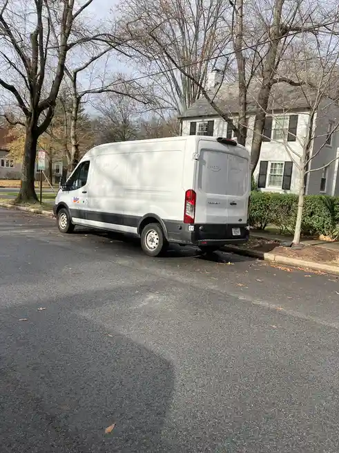 A white Ford Transit van, branded with 'Budget' on the side and 'Amazon' written in marker on the rear doors, is parked on a…