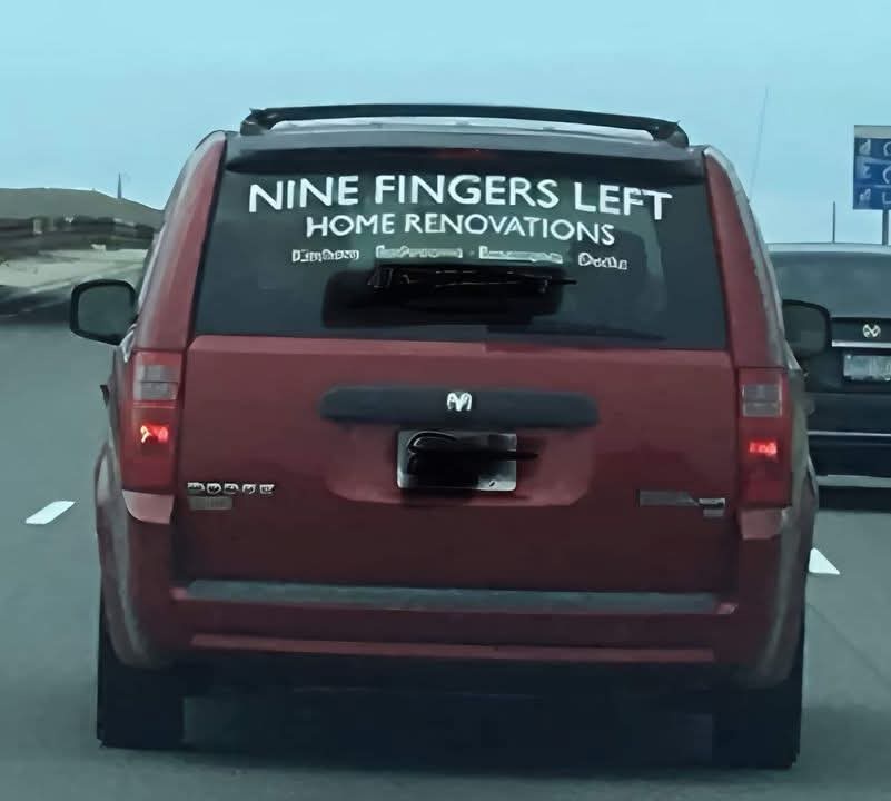 The rear of a red Dodge SUV is shown on a highway, with a large white decal on the back window that reads 'NINE FINGERS LEFT…