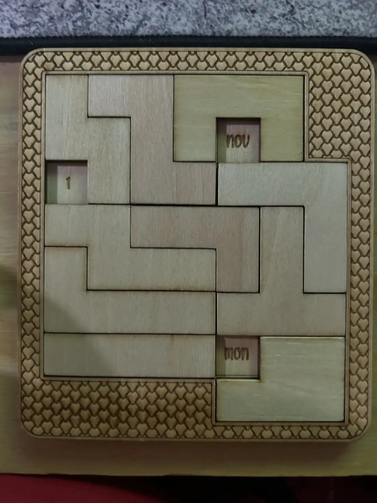 A wooden puzzle with interlocking pieces forms the letters 'you' and 'mon' in recessed slots, with the number '1' visible in…
