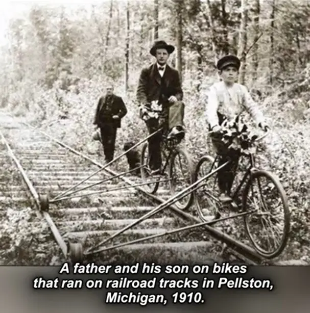 A sepia-toned historical photograph from 1910 shows a man and a boy riding bicycles on railroad tracks in Pellston…