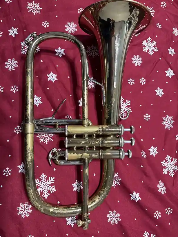 A brass trombone with visible wear and tarnish rests on a red fabric patterned with white snowflakes. The overlaid text…