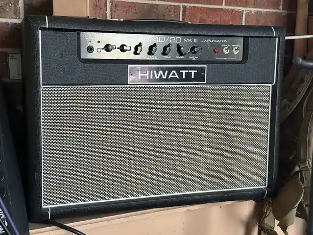 A black Hiwatt T40/20 MK III guitar amplifier head with a silver control panel and grille cloth, mounted against a brick…