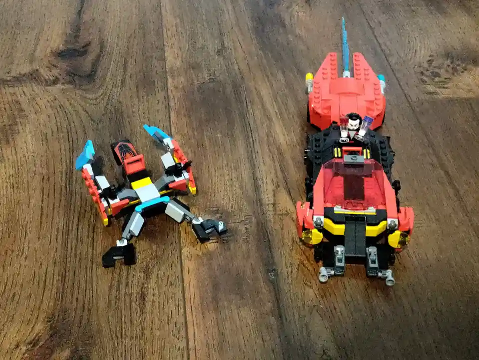 Two LEGO Ninjago sets are shown on a wooden floor, one is a small, broken-looking robot on the left, and the other is a…