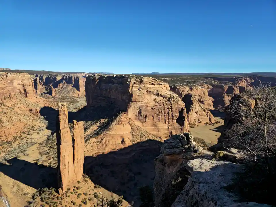 A scenic desert canyon with red rock formations under a clear blue sky, featuring a crescent moon visible in the upper…