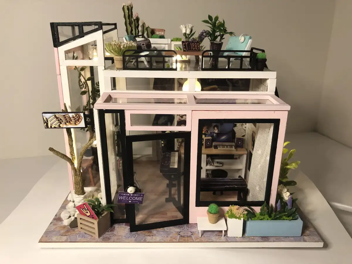 A detailed miniature dollhouse with pink and black framing, glass windows, and a tiled base, featuring tiny furniture…