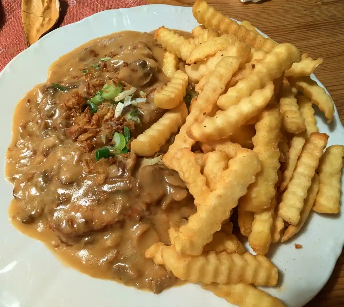 A close-up photo shows a white plate with a serving of meat smothered in a thick, brown gravy with mushrooms and garnished…