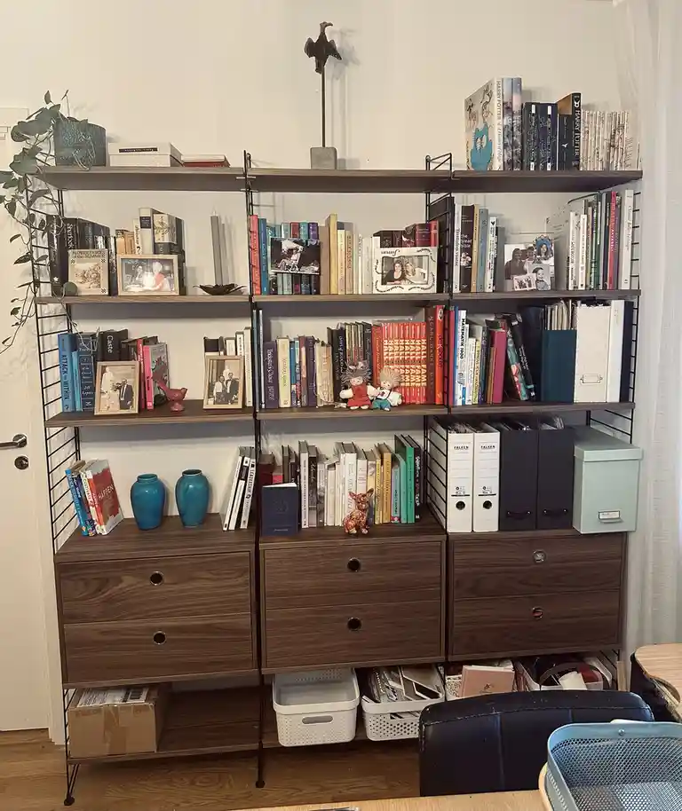 A well-organized, multi-tiered wooden bookshelf filled with books, framed photos, decorative vases, and small figurines…