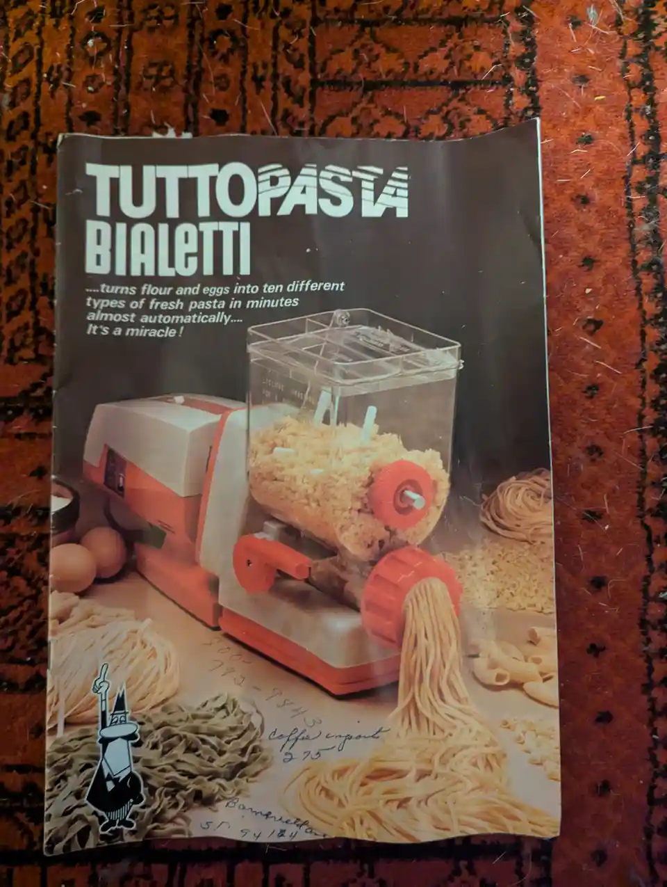A vintage advertisement for a Bialetti Tuttopasta pasta maker, showing an orange and white machine extruding spaghetti while…