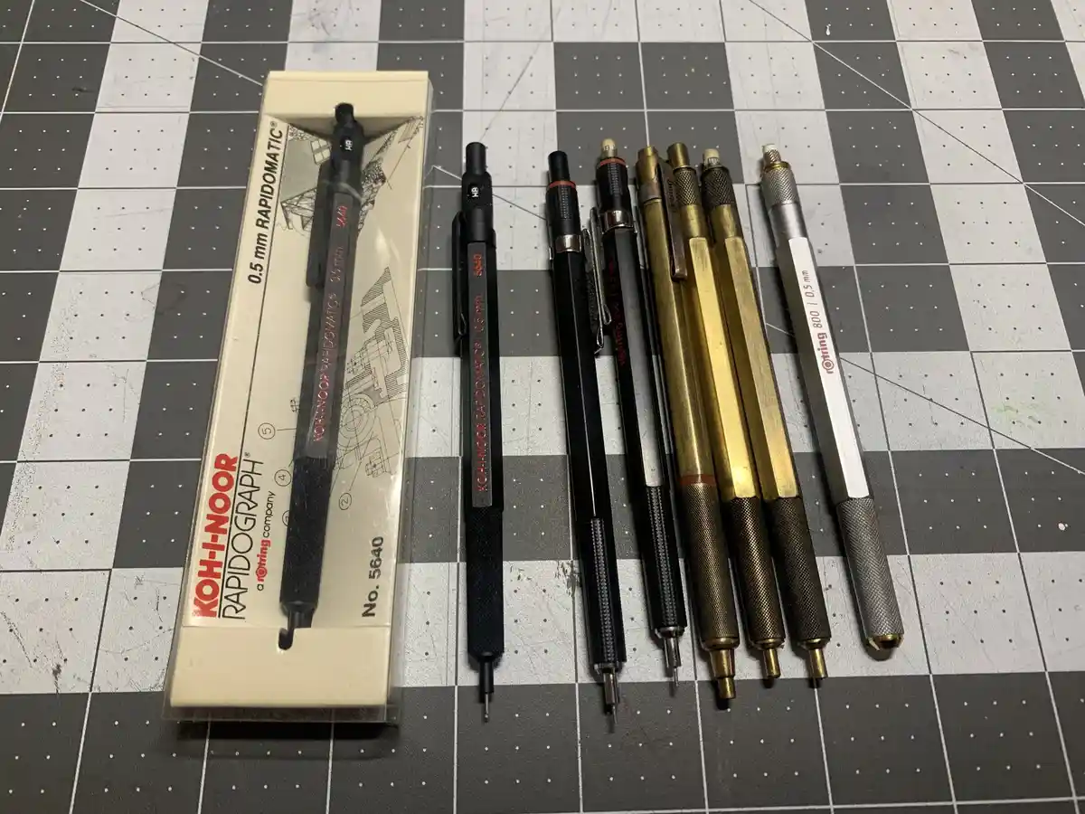 A collection of seven mechanical pencils, including a new Koh-I-Noor Rapidograph No. 5640 in its original packaging, laid…