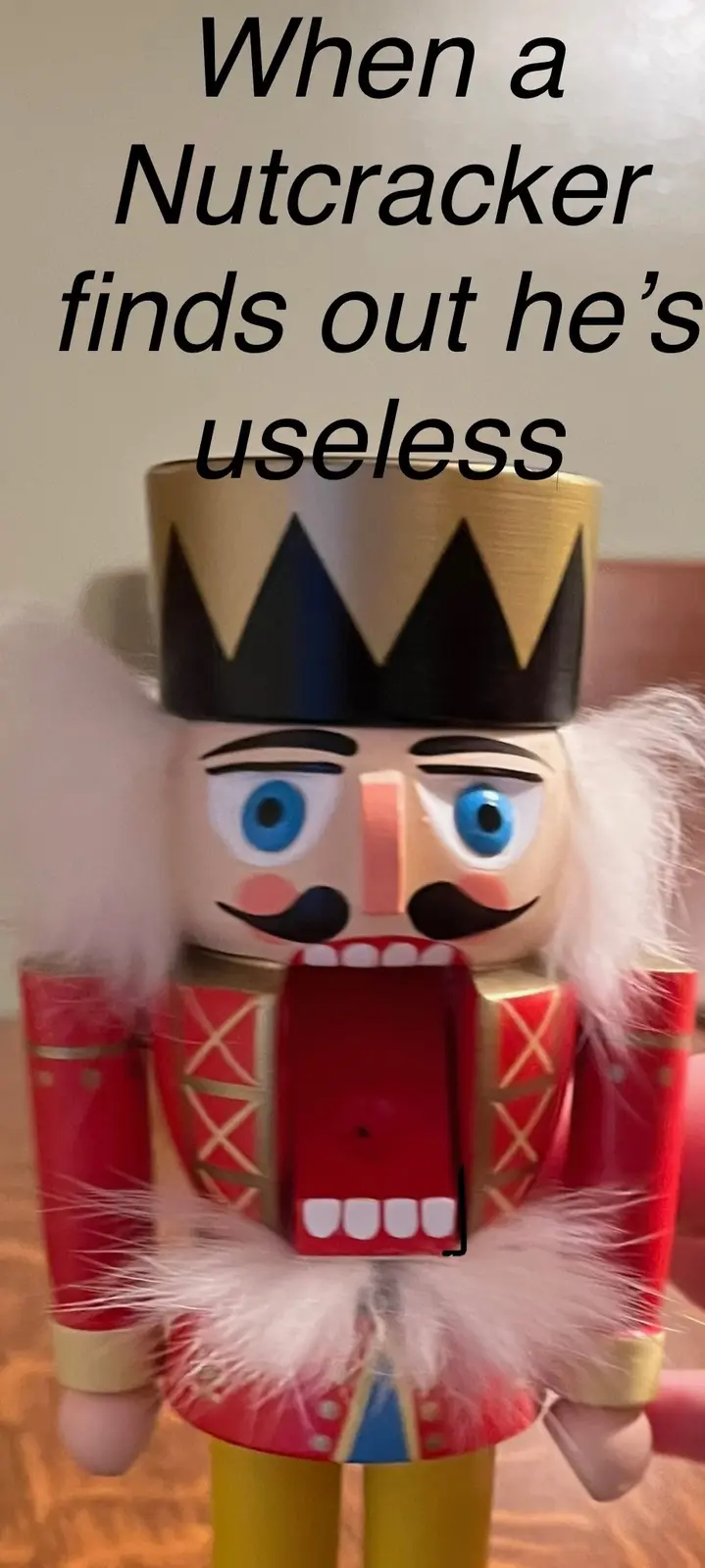 A close-up photo of a traditional wooden nutcracker figurine with a red uniform, gold trim, white feathered collar and…