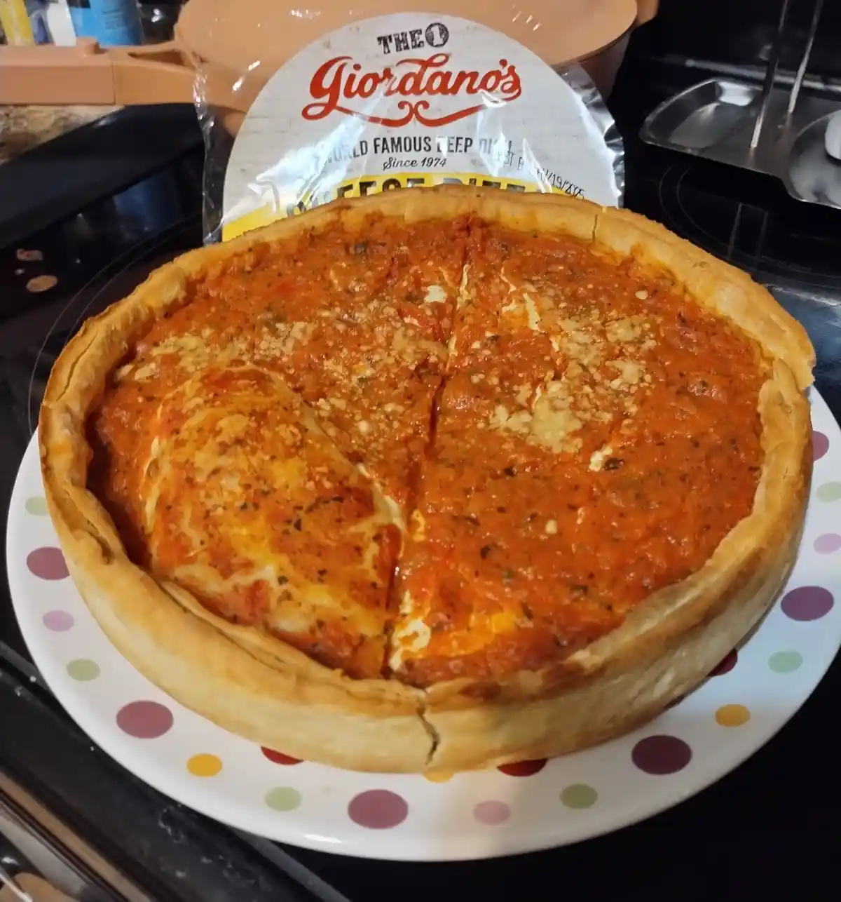 A freshly baked deep-dish pizza from Theo Giordano's sits on a colorful polka-dot plate, with the original packaging visible…