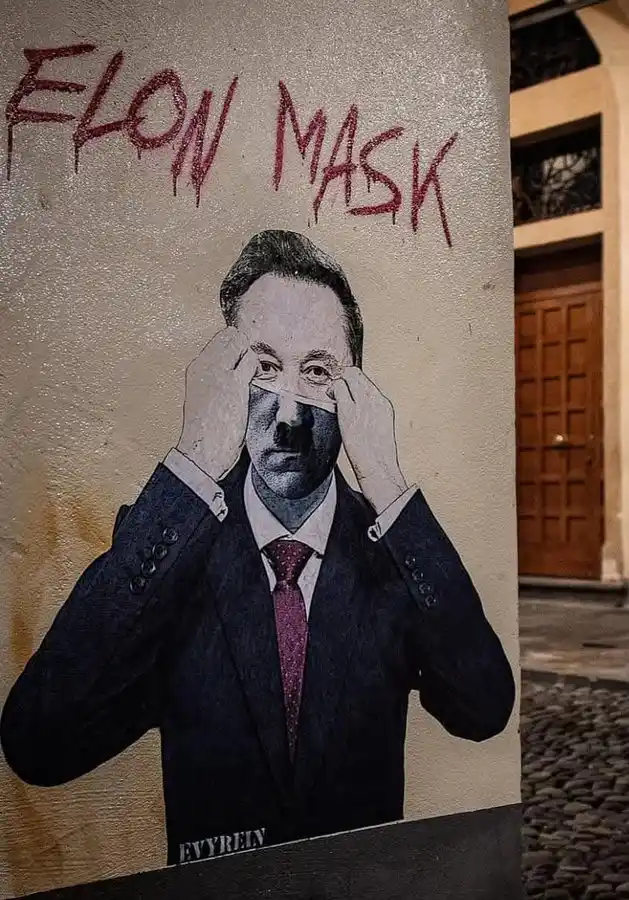 A street mural depicts a man in a suit and tie, with a white tape strip covering his nose and mouth, while he holds the tape…