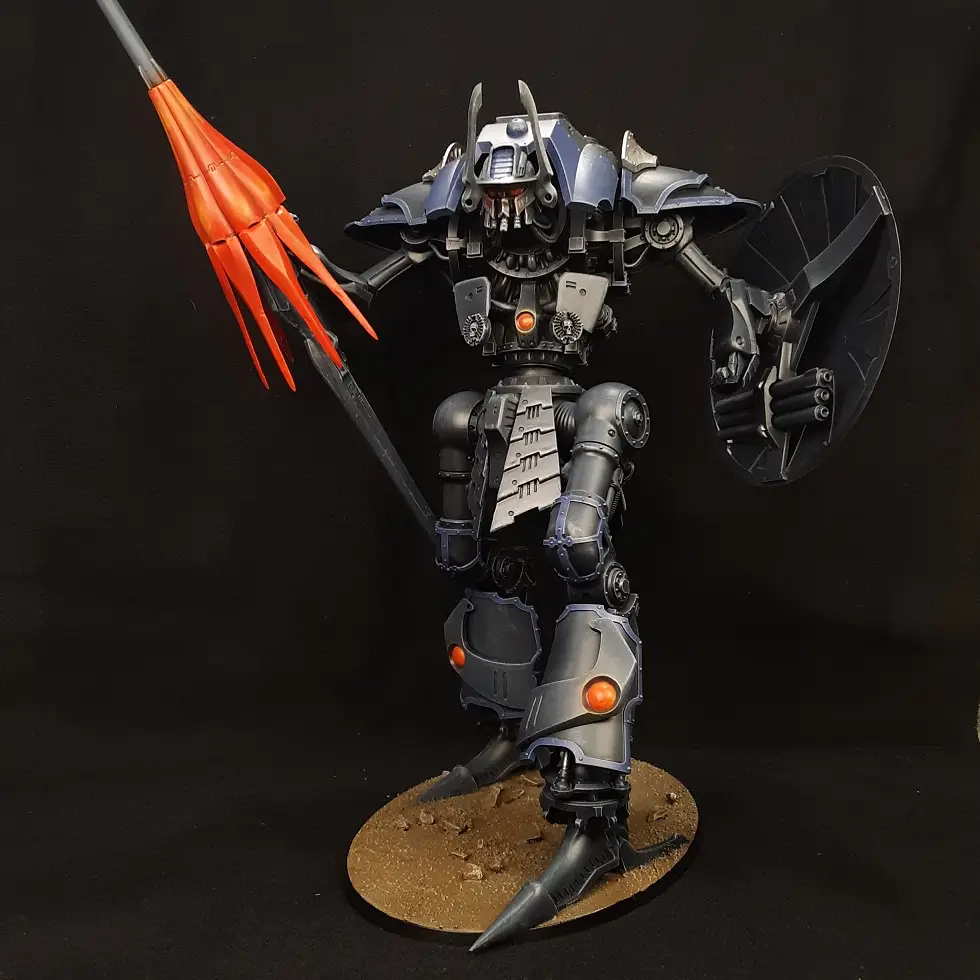 A detailed, painted model of a heavily armored, bipedal robot stands on a circular base against a black background. The…
